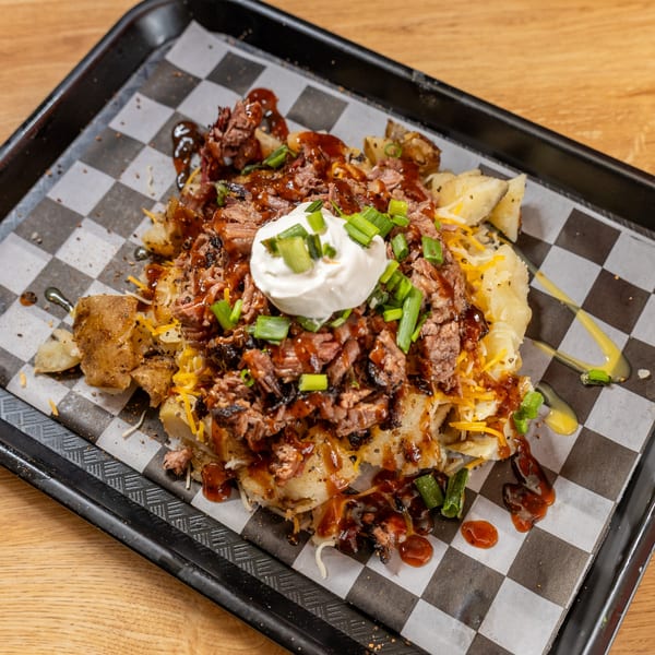 Loaded baked potato with pulled pork, cheese, sour cream, and green onions on a checkered paper.