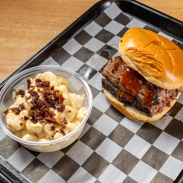 Brisket sandwich with BBQ sauce and a side of mac and cheese topped with bacon bits.