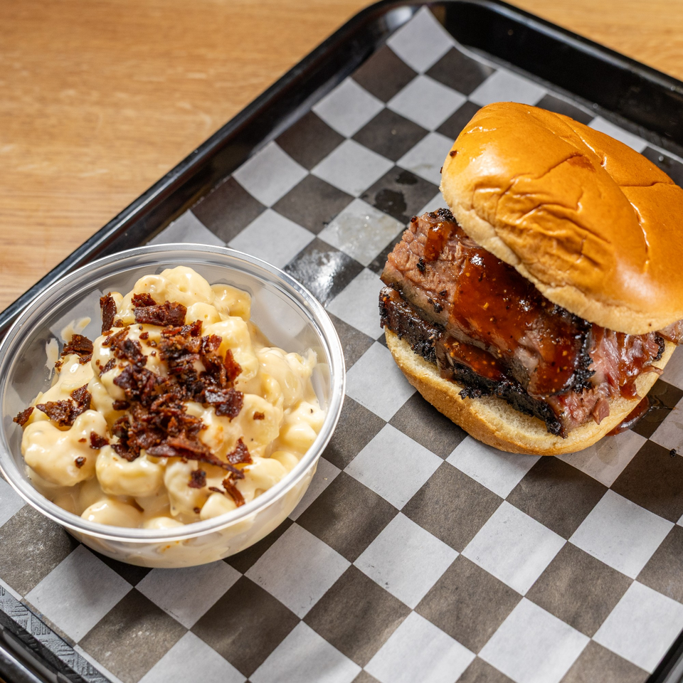 Brisket sandwich with BBQ sauce and a side of mac and cheese topped with bacon bits.