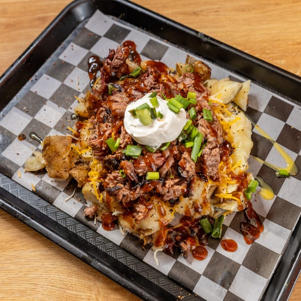 Loaded baked potato with shredded beef, BBQ sauce, cheese, sour cream, and green onions.
